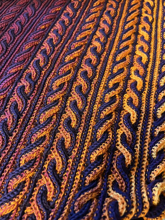 Intricate crocheting showcasing a colorful pattern of twisted and braided stitches in warm orange and purple hues.