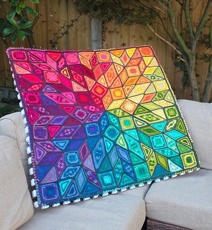 Colorful crocheted blanket with geometric patterns displaying expert crocheting skills in vibrant rainbow hues on a beige couch.