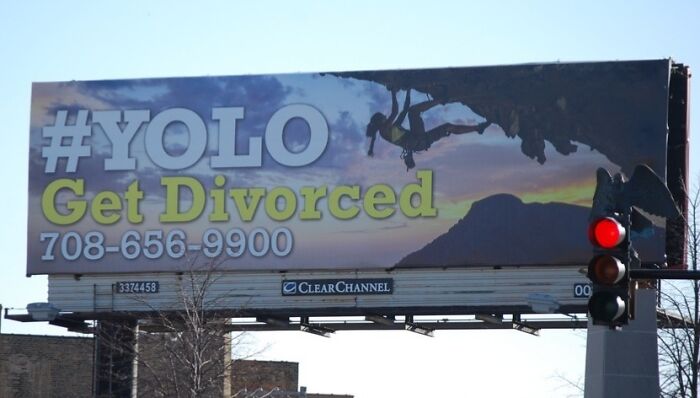 Billboard advertising fail showing rock climbers with text YOLO Get Divorced and a phone number at sunset.