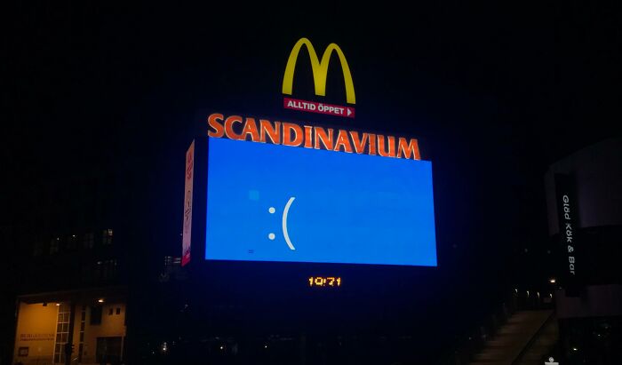 Large digital billboard at night showing a sad face error screen illustrating another unattainable body portrayed in advertising.