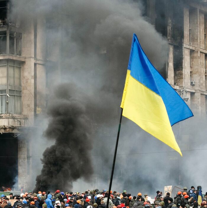 Crowd gathered with smoke rising in background and a prominent Ukrainian flag representing headlines that rocked the world in 2025.