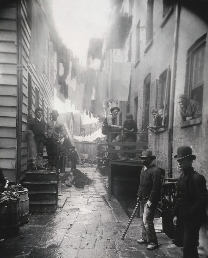 19th century photo showing men in an alley with laundry hanging, capturing a historic moment of daily life.