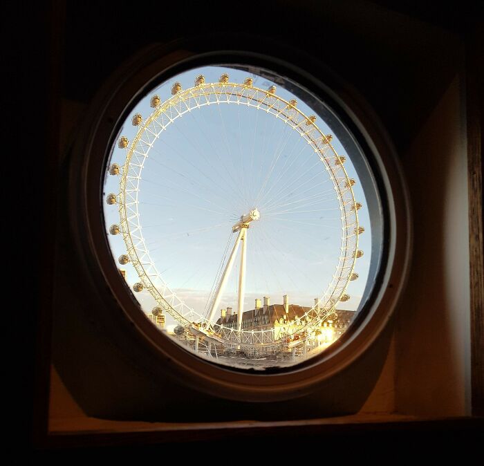 View of a large Ferris wheel through a circular window, showcasing a rare coincidence in perspective and alignment.