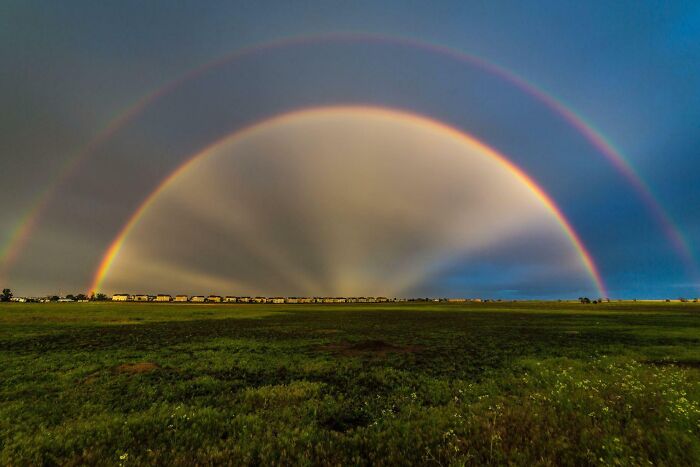 Double rainbow over a green field at sunset showcasing rare coincidences in natural phenomena captured in a photo.