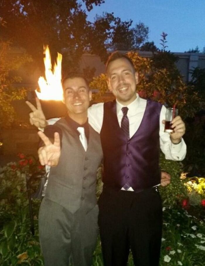 Two men in formal attire smiling and posing with a fire perfectly aligned behind them, a rare coincidence photo.