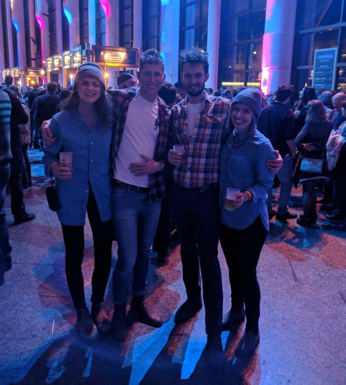 Four friends at a crowded indoor event holding drinks, wearing casual clothes, highlighting rare coincidences in a social setting.