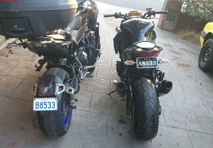 Two motorcycles parked side by side with unusually similar license plates showing a rare coincidence.