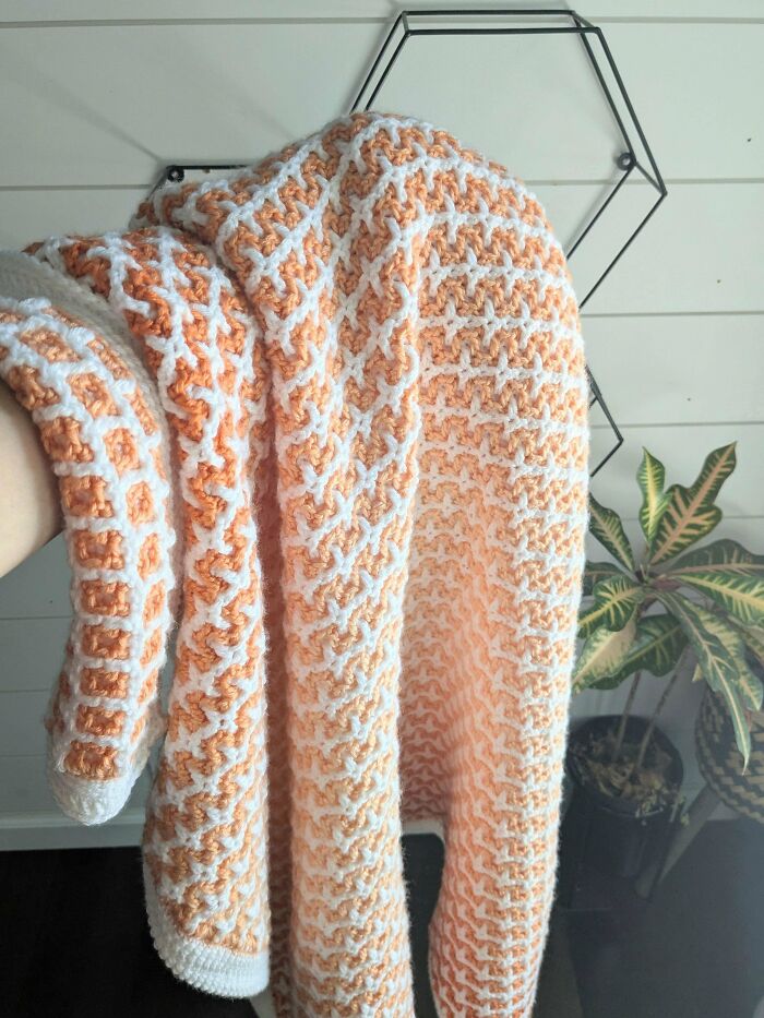 Handmade crochet blanket with peach and white pattern, showcasing intricate crocheting skills and latest projects.