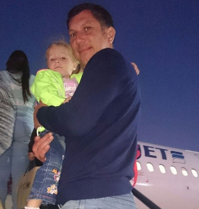 Man holding child near airplane at dusk in a photo taken before disaster, capturing a calm moment before an unfortunate event.