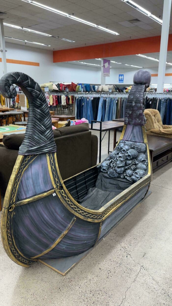Viking ship-themed sled with skull decorations displayed among thrift store furniture and clothing racks.