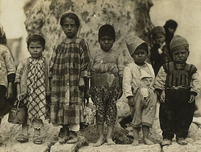 Group of children in worn clothes holding containers, illustrating daily life beyond the WWI trenches in a historic setting.