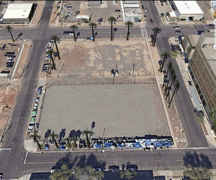 Aerial view of an empty urban lot surrounded by palm trees and tents highlighting lack of affordable housing issues.