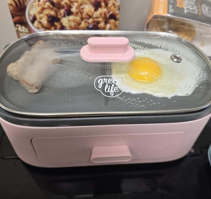 Pink electric cooker cooking an egg and sausage, a dorm kitchen survival guide essential for easy meals beyond cereal.