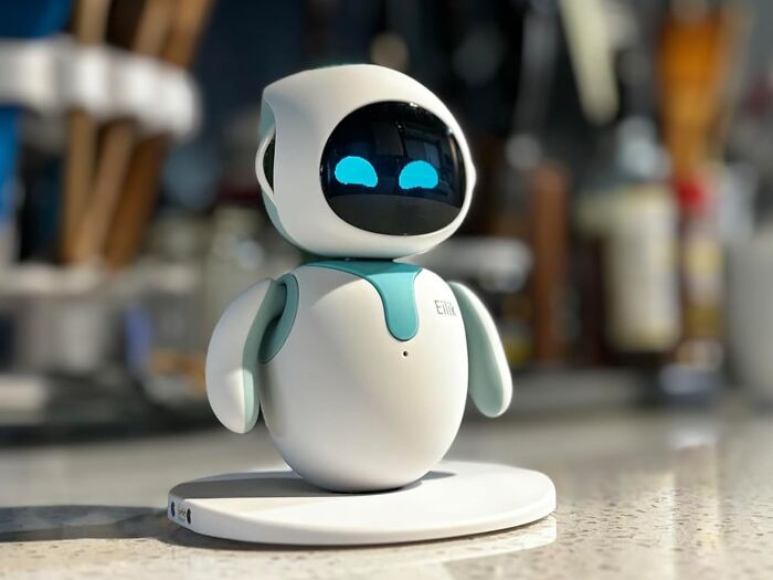 Small white and teal robot with digital blue eyes on a charging base, showcasing an everyday item personality upgrade.