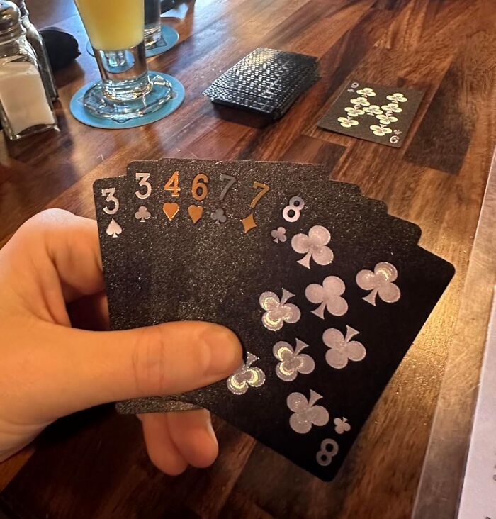 Hand holding black playing cards with sparkling club symbols, showcasing everyday items with a major personality upgrade.