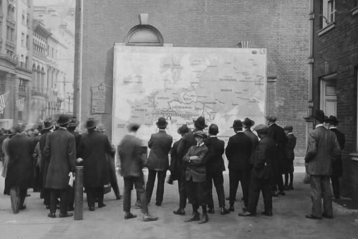 Group of men and boys studying a large map outdoors, showing daily life beyond the WWI trenches during the war.