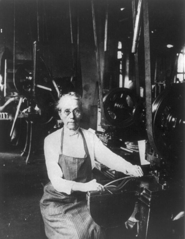 Older woman working with machinery in a factory, showcasing daily life beyond the WWI trenches era.