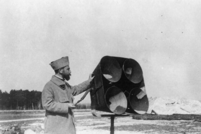 WWI soldier in uniform standing next to large communication device during daily life beyond the trenches.