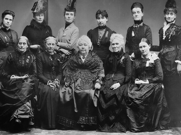Group of women in 1800s America dressed in period clothing, showcasing fashion and social roles of the era.