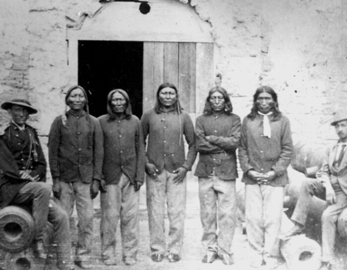 Group of Native American men and soldiers in historic 1800s America, showcasing authentic period clothing and setting.