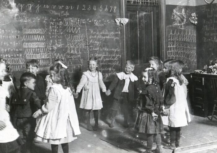 Children holding hands in a classroom setting with chalkboard writings, capturing a gripping picture of 1800s America life.