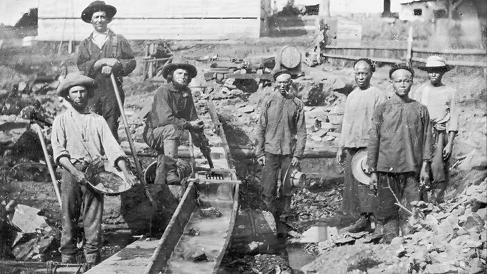 Group of 1800s America workers at a mining site, using pans and sluices to extract minerals from the soil.