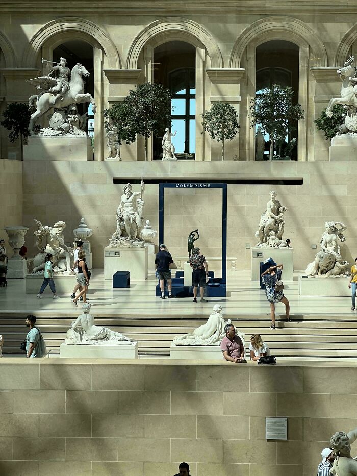 Visitors admiring beautiful accidental renaissance photos and classical sculptures in a bright museum hall with arches.