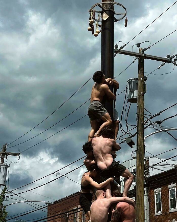 Group of shirtless men climbing a utility pole against a cloudy sky in an accidental renaissance photo style.