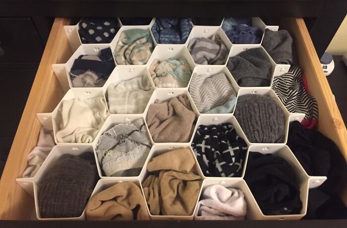 Drawer organizer with hexagonal compartments neatly storing rolled clothes, demonstrating dorm storage solutions for awkward nooks.