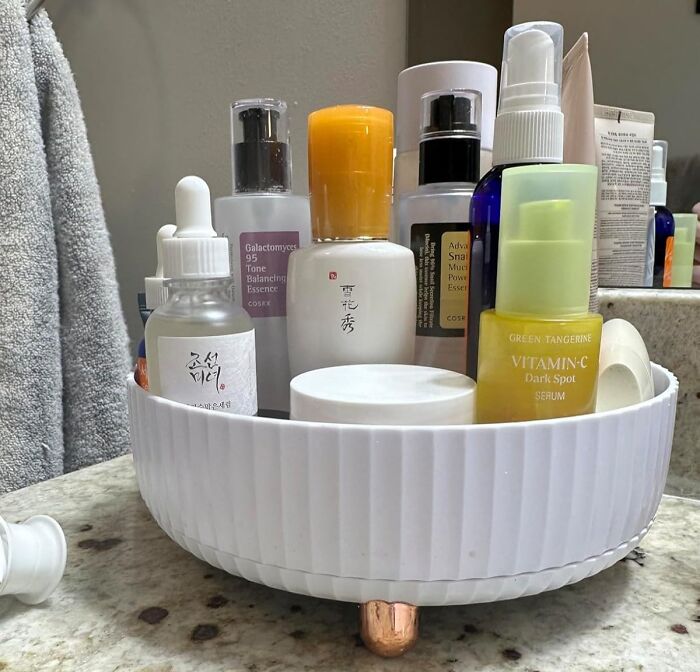 Rotating storage organizer on bathroom counter neatly holding various skincare bottles to maximize dorm storage space.