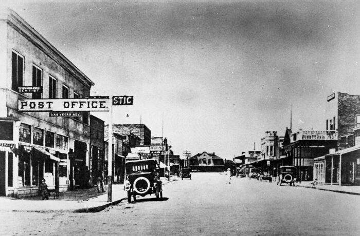 Historic black and white street view of early Vegas featuring vintage cars and buildings including a post office.