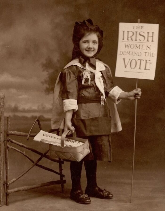 Young girl dressed in suffrage era clothes holding a sign demanding Irish women’s right to vote in the 20th century.