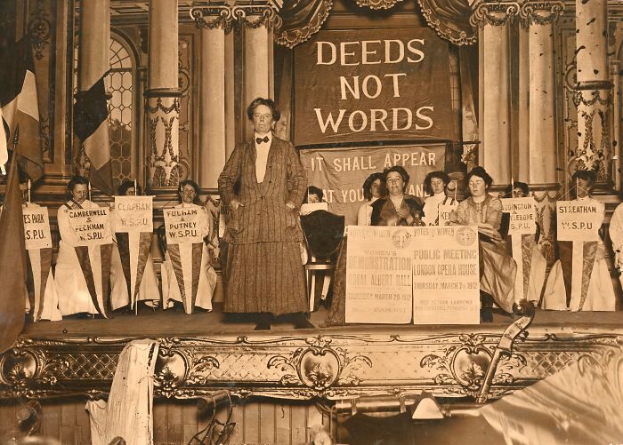 Women in the 20th century suffrage era standing on stage with banners advocating votes for women and equal rights.