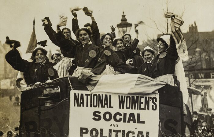 Group of women in the 20th century suffrage era celebrating on a vehicle with a National Women’s Social and Political banner.