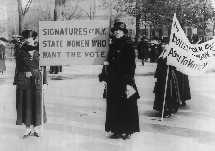 Women in the 20th century suffrage era holding signs advocating for voting rights during a public demonstration.