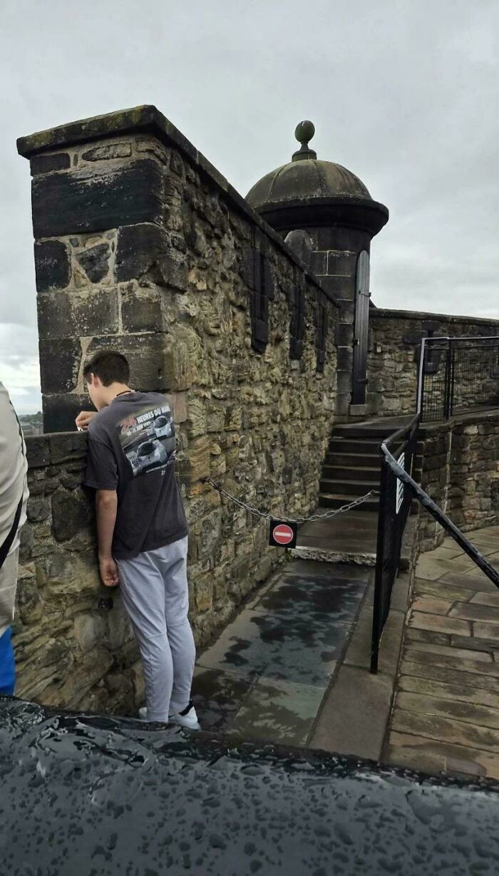 A person ignoring rules and etiquette by leaning over a restricted area behind a chain barrier at a stone structure.