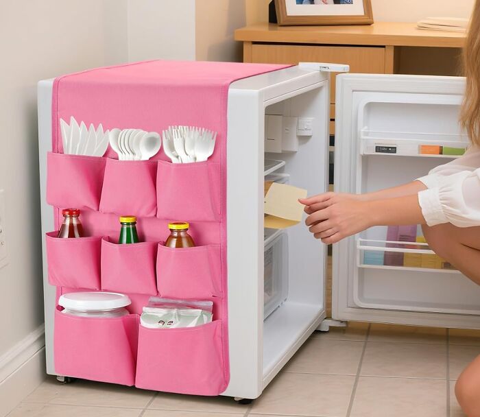 Small dorm kitchen setup with a mini fridge and pink organizer holding utensils and bottles nearby.