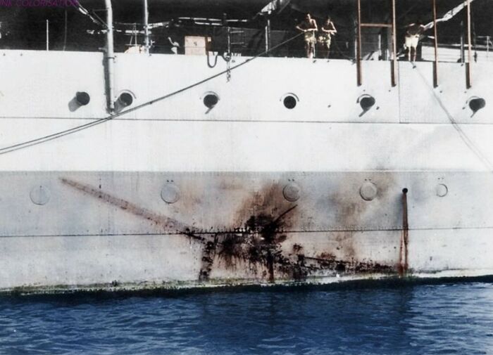 Ship hull with large rust stain floating on calm water in a historical photo with unusual wear marks visible.