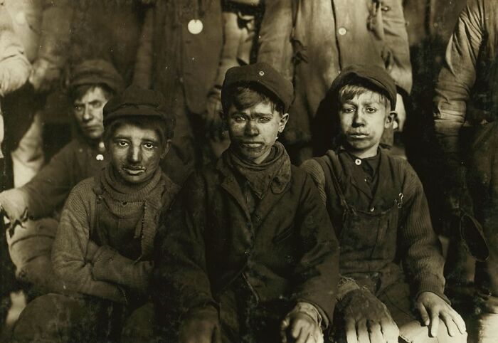 Group of young boys with dirty faces and worn clothing in a historical photo showcasing child labor conditions.