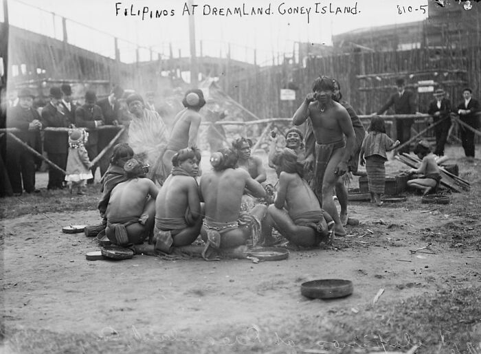 Group of indigenous Filipinos wearing traditional attire gathered around a fire at Dreamland, an unusual historical photo from the past.
