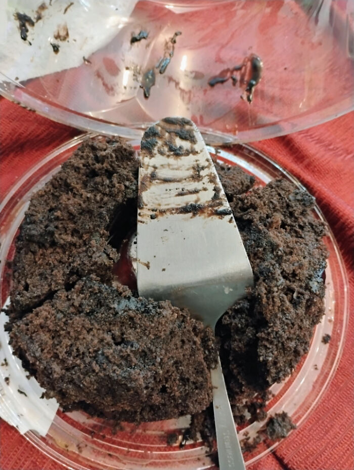 Partially eaten chocolate cake left in plastic container with dirty spatula, showing lack of care about rules and etiquette.