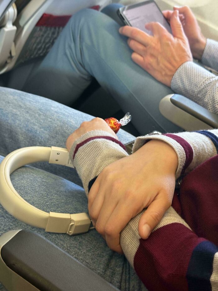 Hands of a person holding a candy, resting on headphones placed on a lap, showing disregard for airplane etiquette.