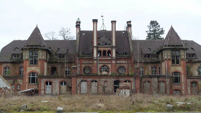 Abandoned place with a large, decaying brick mansion surrounded by overgrown grass and broken windows in a desolate area