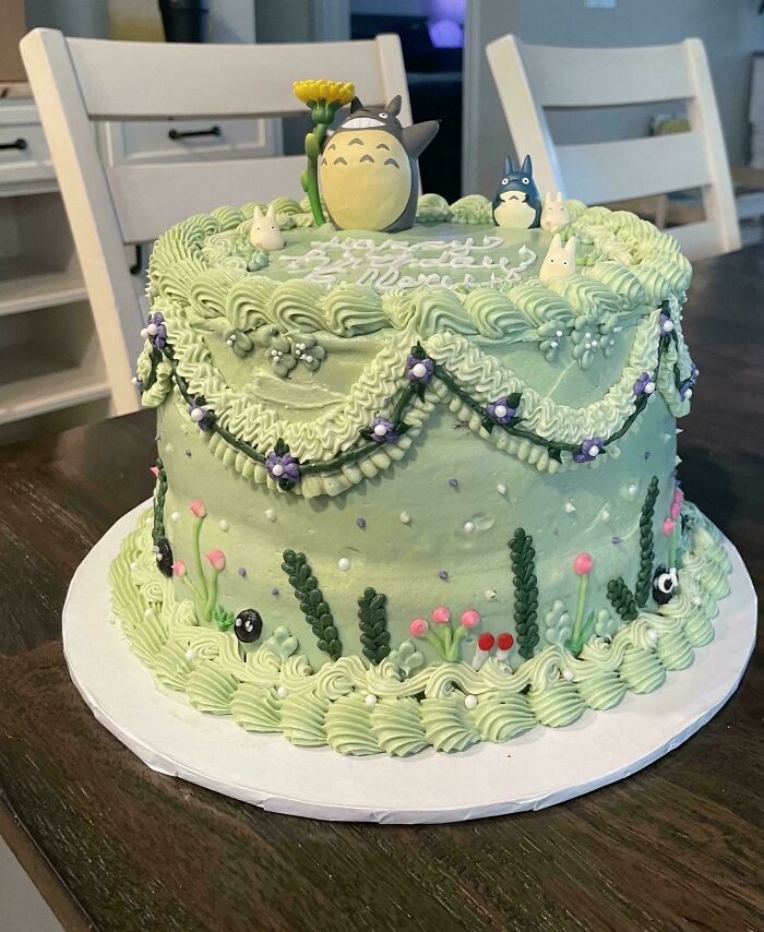 Green frosted cake decorated with Totoro figures and floral designs, showcasing gorgeous baked goods artistry.