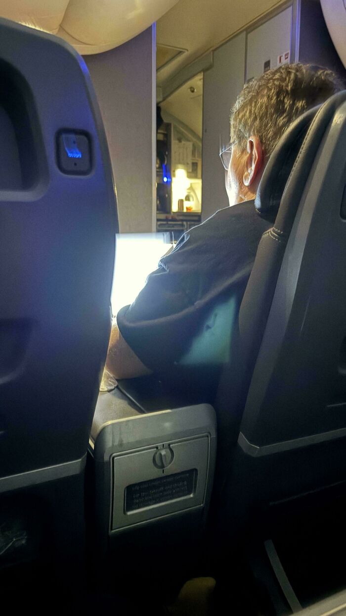 Passenger on a plane using a glowing laptop screen that disturbs others, showing disregard for rules and etiquette.