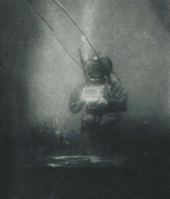 Underwater vintage diver in old deep-sea suit holding a sign, one of the weird historical photos from the past.