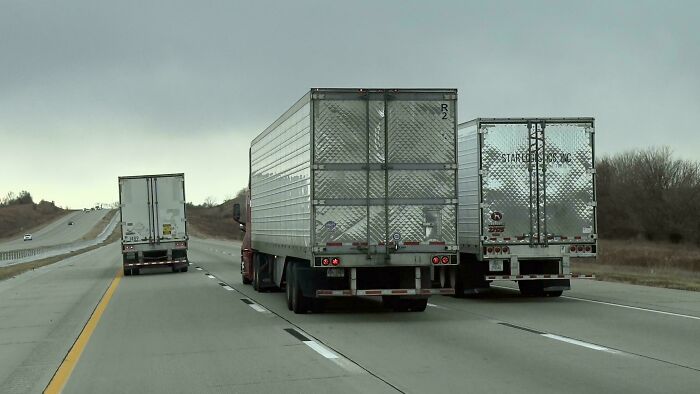 Two large trucks driving side by side on a highway, blocking lanes and showing no care for rules or etiquette.