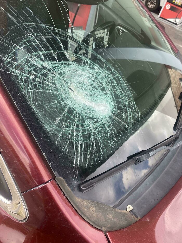 C*****d car windshield with a large circular impact, showing people who have no care about rules and etiquette.