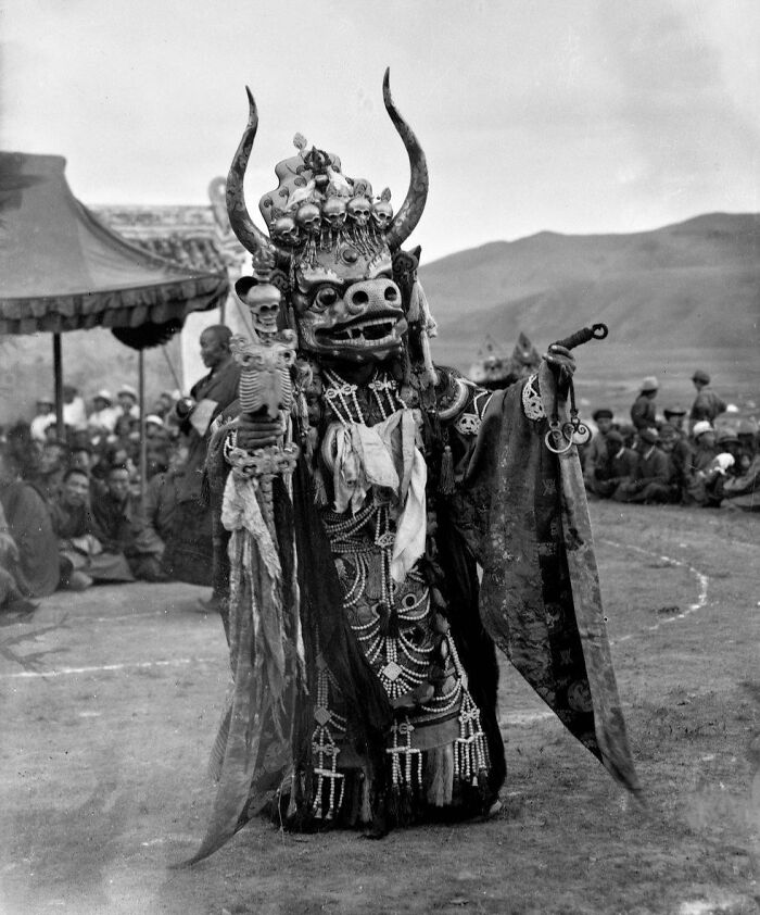 Masked performer in traditional costume with skulls and horns at a cultural event, a striking historical photo.