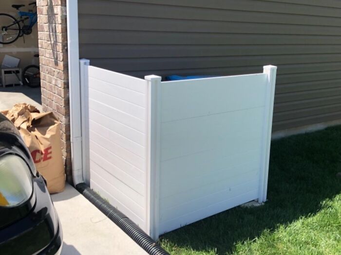 White privacy fence installed around trash bins to hide ugly outdoor clutter with simple genius hacks for yard organization.